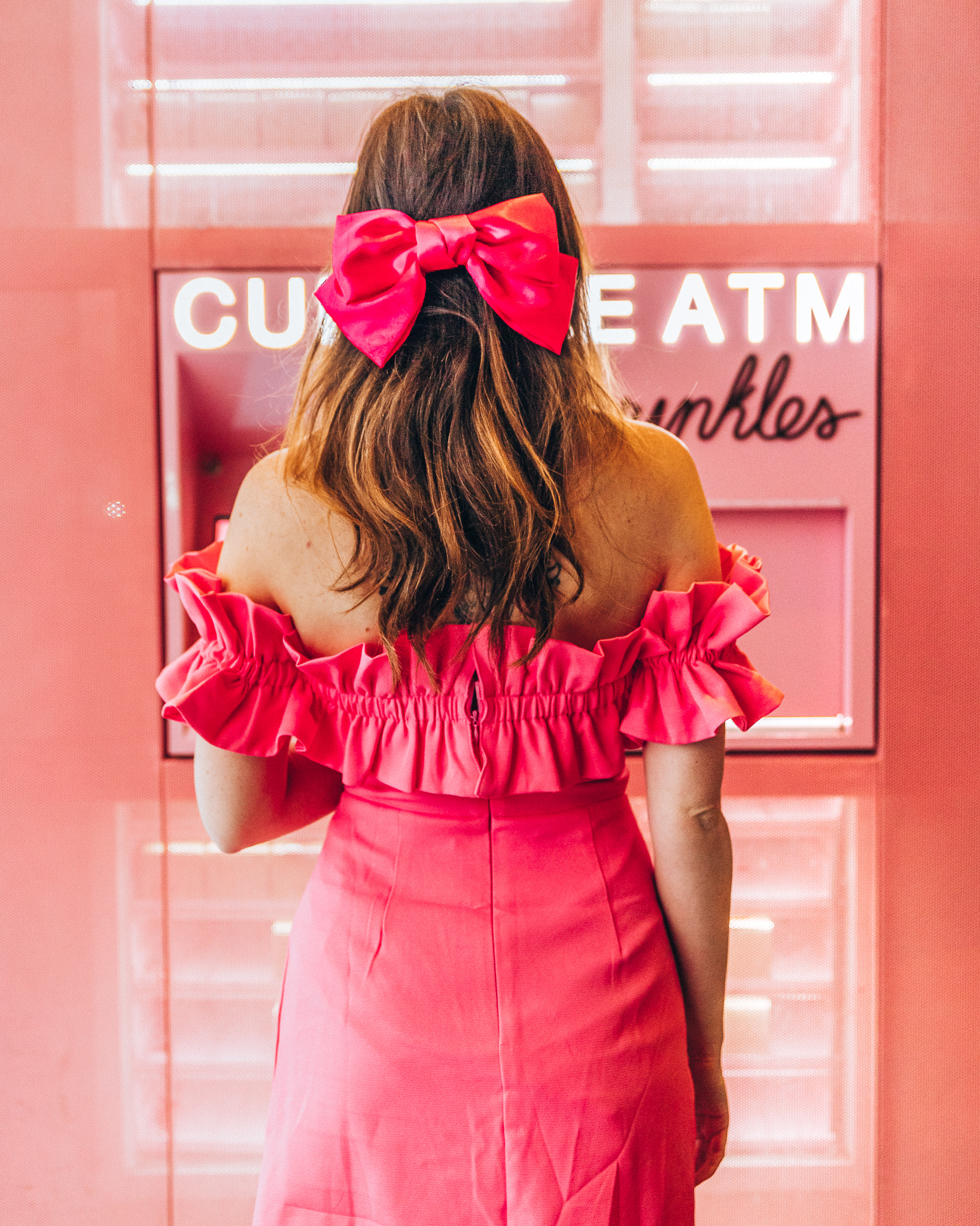 Woman with a pink bow and pink dress facing the cupcake atm